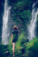 Obraz premium Young woman posing on a great Sekumpul waterfall in the deep rainforest of Bali island, Indonesia.