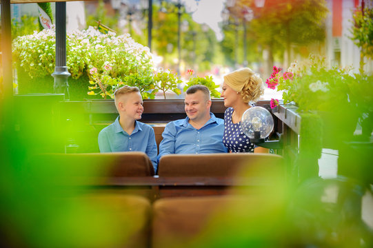 family is resting in a street cafe, sitting at a table and talking