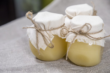 Three glass jars full of honey covered with cloth on a linen fabric.