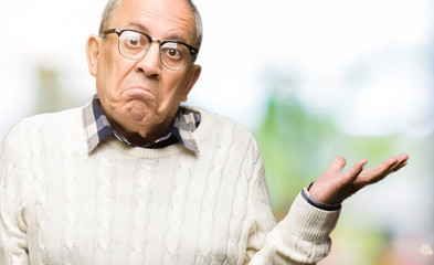 Handsome senior man wearing glasses and winter sweater clueless and confused expression with arms...