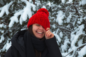 portrait of young smiling woman in winter clothes in red hat with bubo fir tree in background