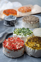 Assortment of French fresh white soft goat cheeses with different tastes topping made with herbs, paprika, indian curry, bruscetta, chives and dried tomatoes