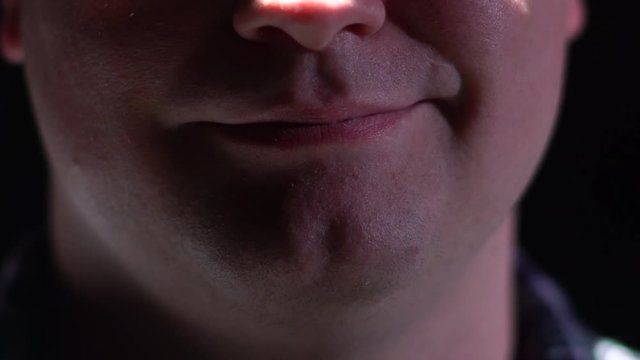Close up of a man smirking under dramatic studio lighting.