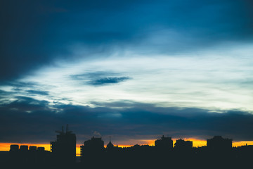 Cityscape with wonderful varicolored vivid dawn. Amazing dramatic blue cloudy sky above dark silhouettes of city buildings. Atmospheric background of orange sunrise in overcast weather. Copy space.