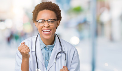 Young african american doctor woman wearing medical coat over isolated background very happy and excited doing winner gesture with arms raised, smiling and screaming for success. Celebration concept.