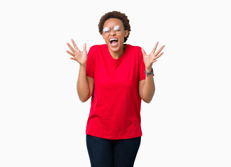 Beautiful young african american woman wearing glasses over isolated background celebrating mad and crazy for success with arms raised and closed eyes screaming excited. Winner concept