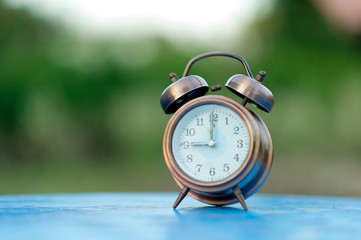 Golden alarm clock picture placed on a blue table, green background Punctual concept With copy space