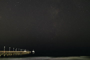 Night landscape. Small pleasure boat moored to a pier near the sea coast. Starry night sky over the sea.