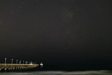 Poster de jardin Côte Night landscape. Small pleasure boat moored to a pier near the sea coast. Starry night sky over the sea.