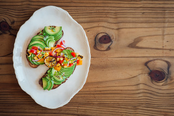 Top shot of sliced avocado on rye toast with a rustic tomato, yellow pepper and red onion salsa and burnt lime, on a wooden background with free text space