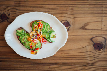 Top shot of sliced avocado on rye toast with a rustic tomato, yellow pepper and red onion salsa and burnt lime, on a wooden background with free text space