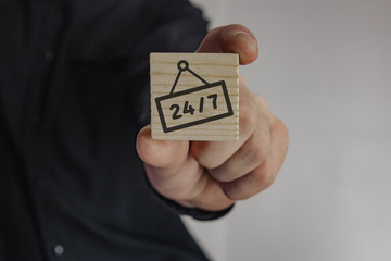wooden cube in the hand of a man with the inscription 24/7