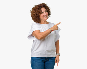 Beautiful middle ager senior woman wearing white t-shirt over isolated background cheerful with a smile of face pointing with hand and finger up to the side with happy and natural expression on face