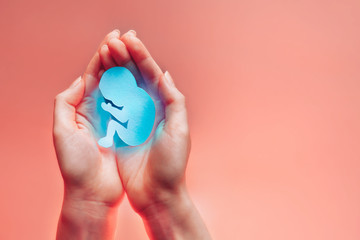 Womans palms pressed together and keep paper embryo with blue light (protection or death). Hands on...