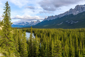 Bow River Valley - A Spring evening view of Bow River winding through dense pine forest at base of rugged mountains of South Banff Ranges in Banff National Park, Alberta, Canada.