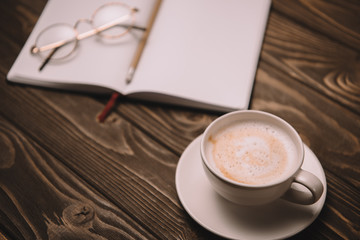 close up of cappuccino, notebook and eyeglasses on wooden table