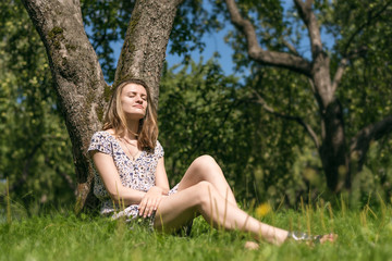 Naklejka na ściany i meble Attractive young woman resting under a tree in the spring garden