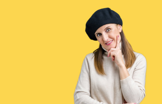 Middle age mature woman wearing winter sweater and beret over isolated background with hand on chin thinking about question, pensive expression. Smiling with thoughtful face. Doubt concept.
