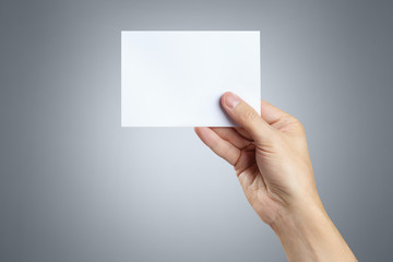 Obraz premium Male hand holding a blank card 10x15cm on gray background