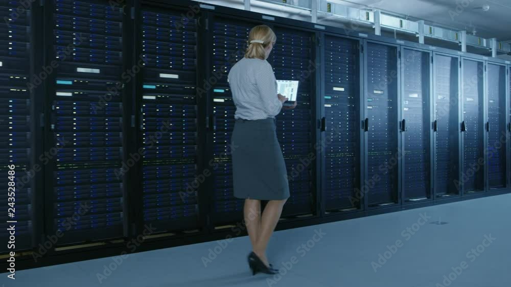 Poster In Data Center: Female IT Specialist Walks along the Row of Operational Server Racks, Uses Laptop to Run Maintenance Programme. Modern High-Tech Telecommunications Operational Data Center.