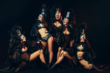 The group of young happy smiling beautiful female dancers with carnival dresses posing on black studio background