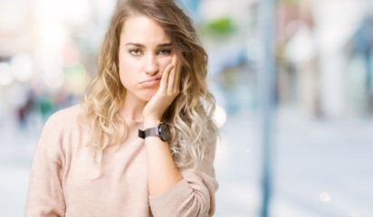 Beautiful young blonde woman wearing sweatershirt over isolated background thinking looking tired and bored with depression problems with crossed arms.