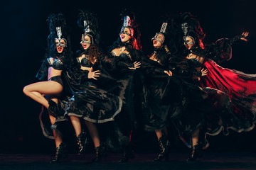 The group of young happy smiling beautiful female dancers with carnival dresses posing on black studio background