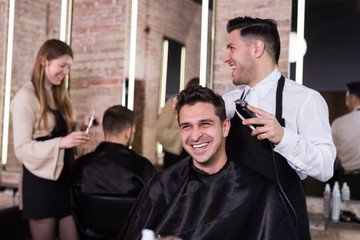 Hairdresser man doing styling of guy with electric hair clipper