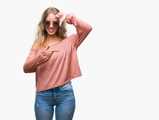 Beautiful young blonde woman wearing retro sunglasses over isolated background smiling making frame with hands and fingers with happy face. Creativity and photography concept.