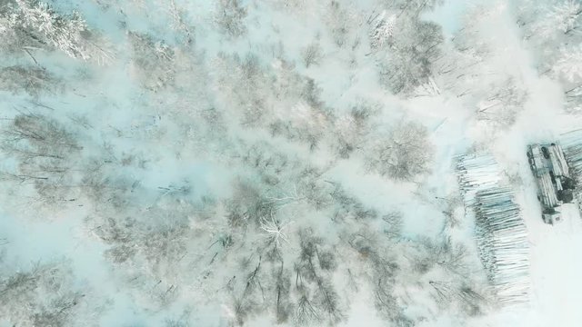 Industrial wood production concept: a log loader or forestry machine loads a log truck in winter, aerial video.
