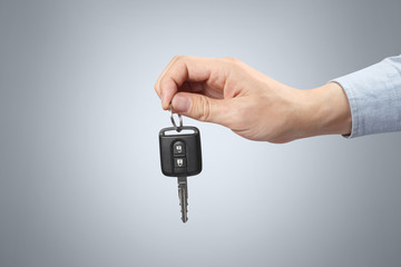 Hand holding a car key on gray background