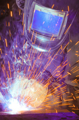  Welder on the production of weld metal. Sparks fly, smoke