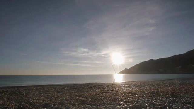 Senior man paints a picture on the beach. Elderly male artist removes the painting from the easel and goes away on raising over seashore and mountains sun background.