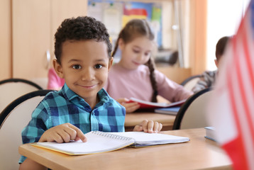 Cute African American boy doing homework in classroom at school