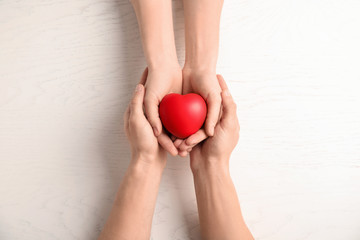 People holding red heart on wooden background, top view. Cardiology concept