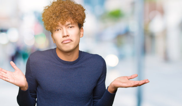 Young handsome man with afro hair clueless and confused expression with arms and hands raised. Doubt concept.