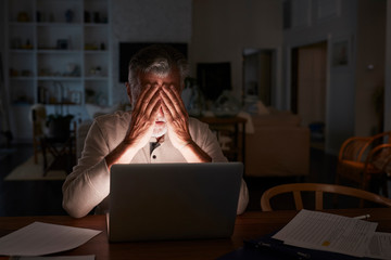 Senior Hispanic man checking his finances online at home using a laptop computer at night