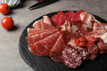 Slate plate with different meat delicacies on gray table