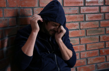 Young addicted man sitting near brick wall after using drugs