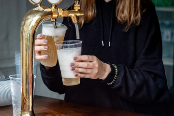 A bartender serving beer at a dispenser in plastic glasses - Image