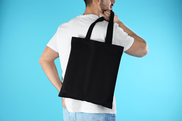 Young man holding textile bag on color background, closeup. Mockup for design
