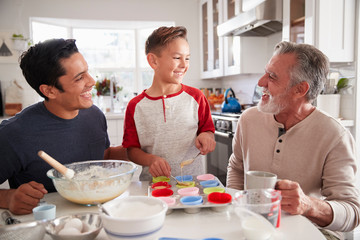 Three male generations of family making cakes together at the table in the kitchen, close up