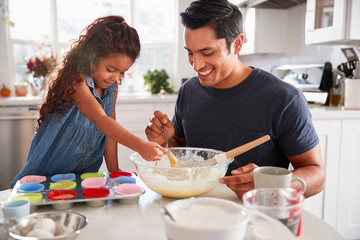 Young girl standing at the kitchen table preparing a cake mix with her father, close up