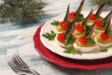 Eggs stuffed with sprats and red caviar on a white plate. Festive snack 