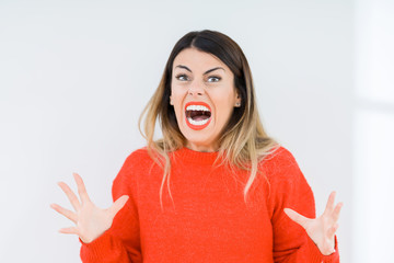 Young woman wearing casual red sweater over isolated background crazy and mad shouting and yelling with aggressive expression and arms raised. Frustration concept.