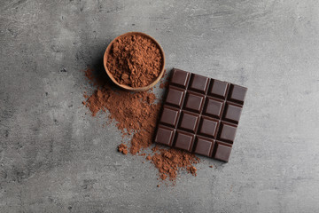 Chocolate bar and cocoa powder on grey background, flat lay