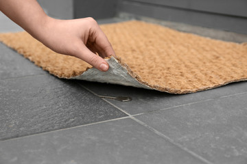 Woman lifting door mat to reveal key hidden underneath, closeup. Space for text