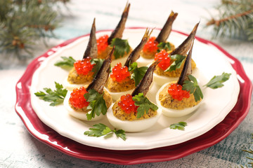Eggs stuffed with sprats and red caviar on a white plate. Festive snack 