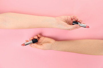 Women holding lipsticks on color background, top view