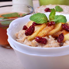 Porridge with caramelized apples and dried cranberries topped with mint surrounded by breakfast ingredients